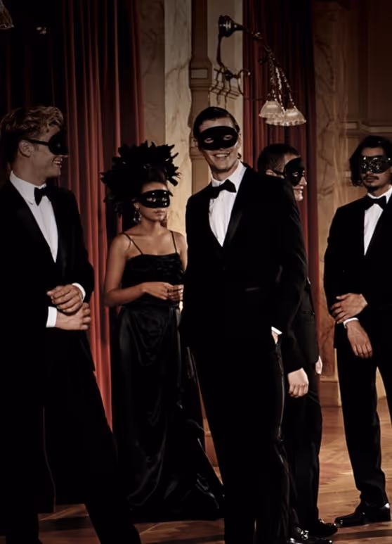 Group of five people dressed in formal black attire with black masquerade masks at an elegant indoor event.