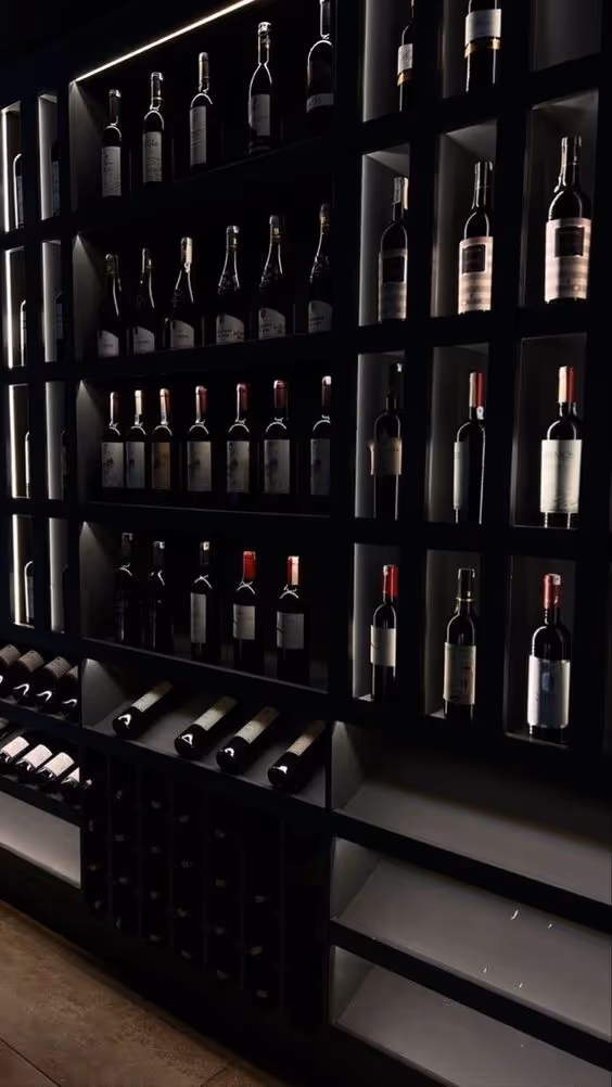 Dimly lit wine rack with multiple bottles of red and white wine arranged in cubbyholes and horizontal slots.