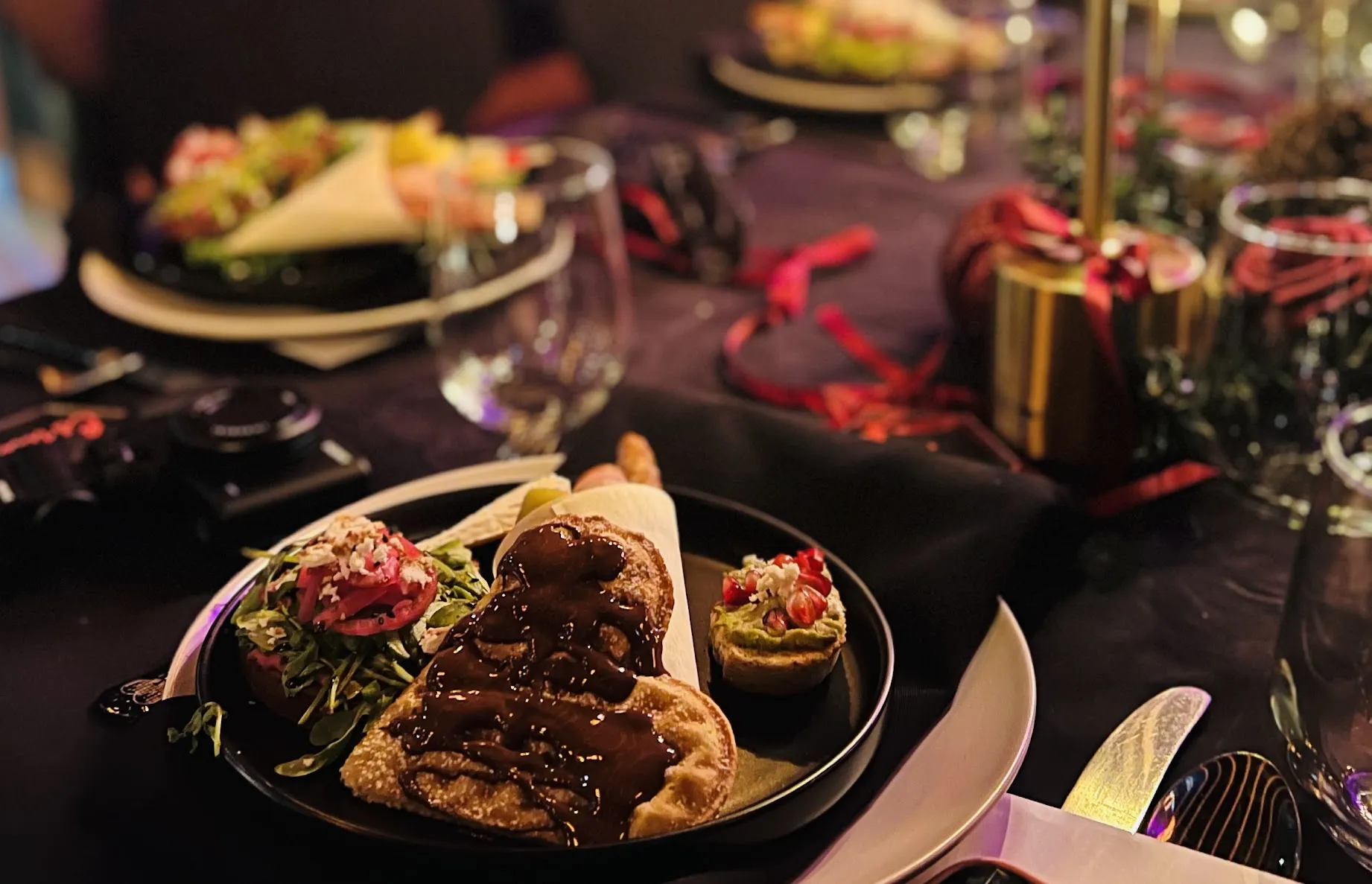 Plate with dessert drizzled in chocolate, salad with greens and pickled onions, and small tart topped with pomegranate.
