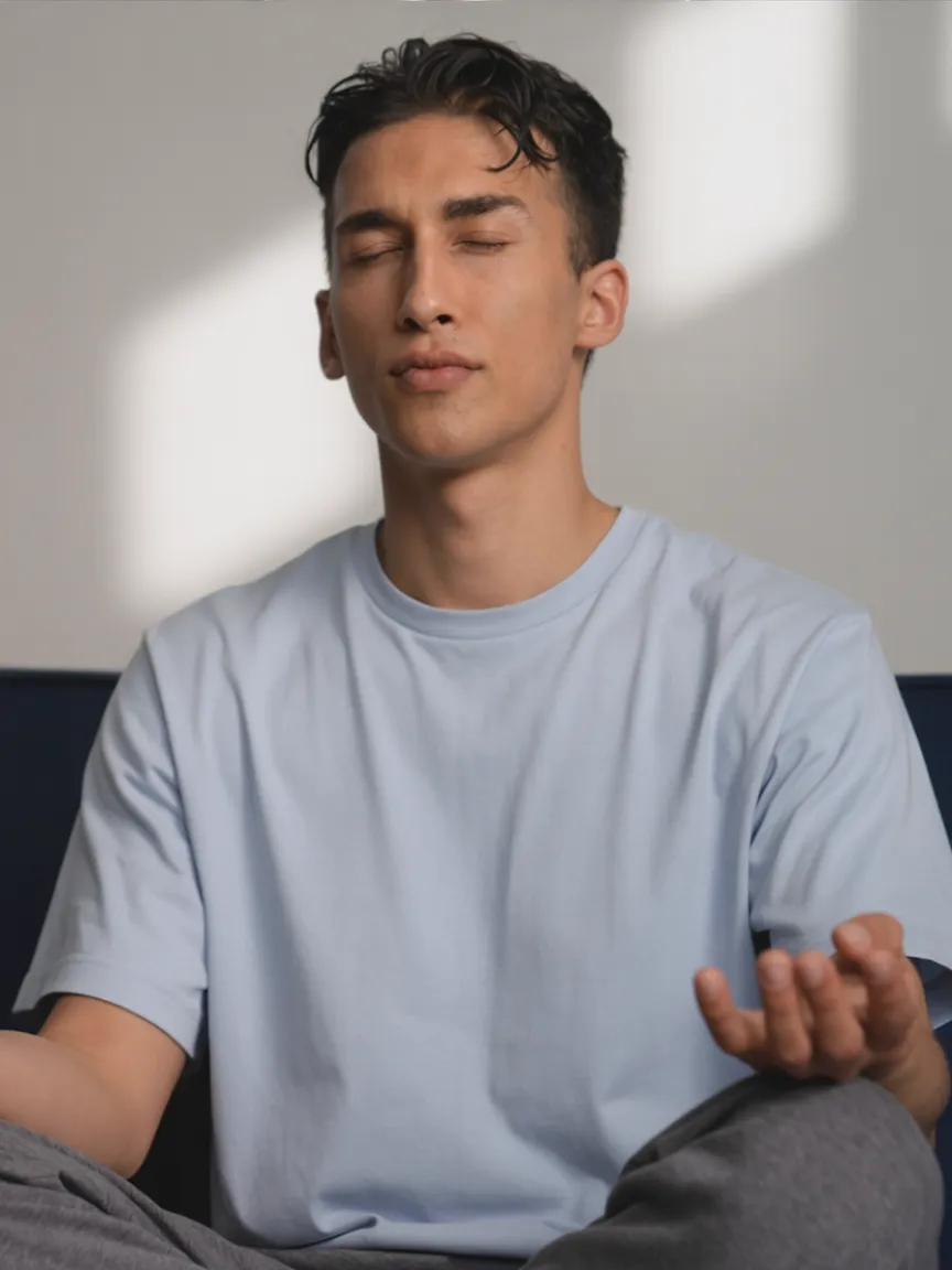 Man with closed eyes sitting cross-legged, meditates with open hand resting on knee.
