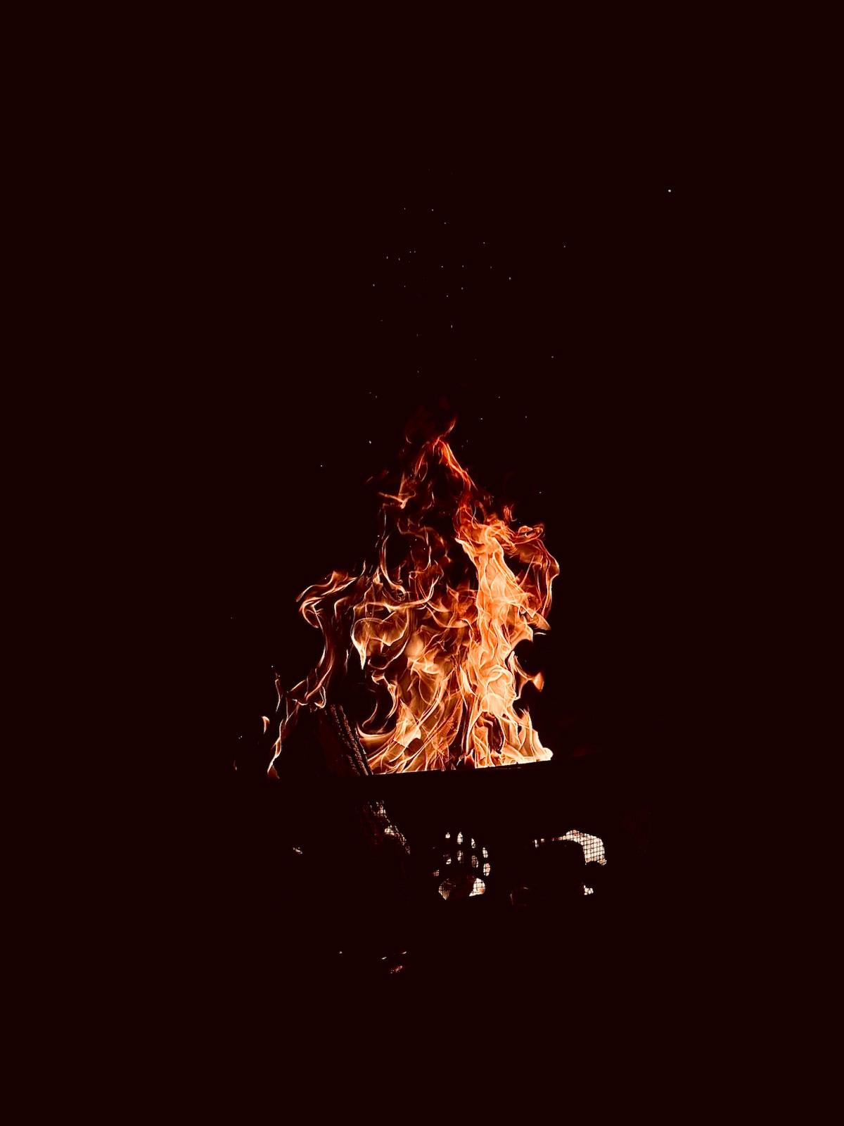 Bright orange flames rising from a dark fire pit against a black background at night.