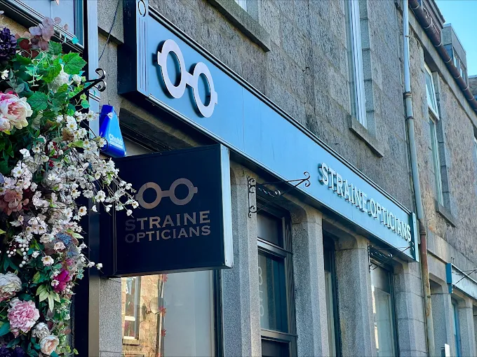 Straine Opticians storefront with glasses logo and decorative flower arrangement