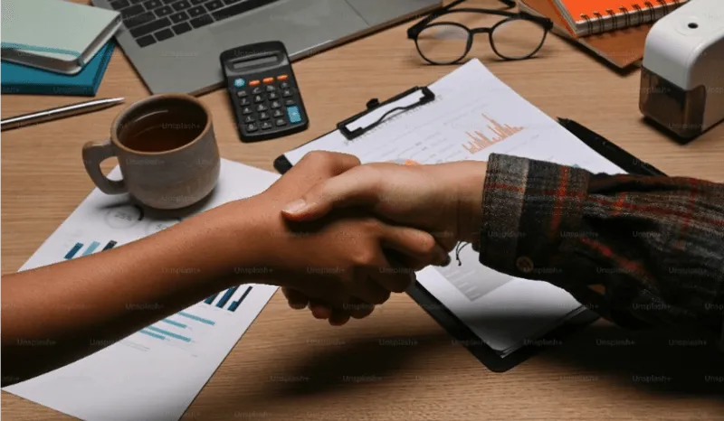 Two people shaking hands in front of a laptop.