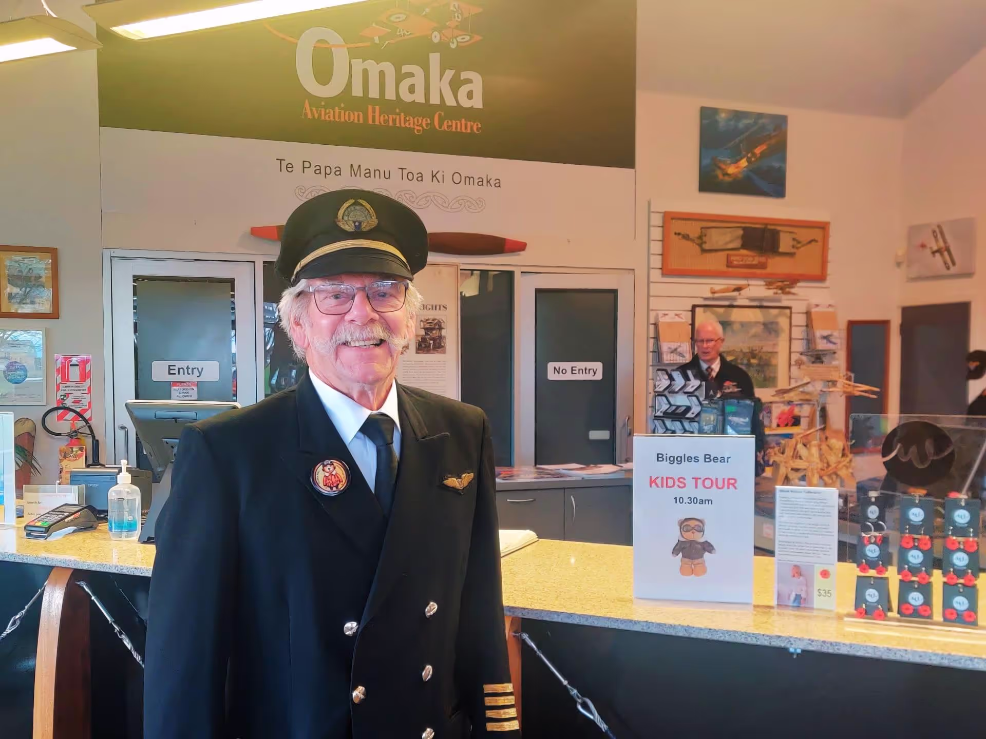 A person in a pilot uniform standing at the Omaka Aviation Heritage Centre reception desk.