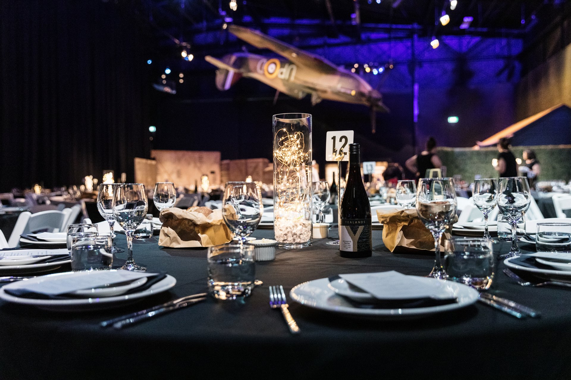 Elegant gala dinner setup with tables and hanging vintage airplane in background.