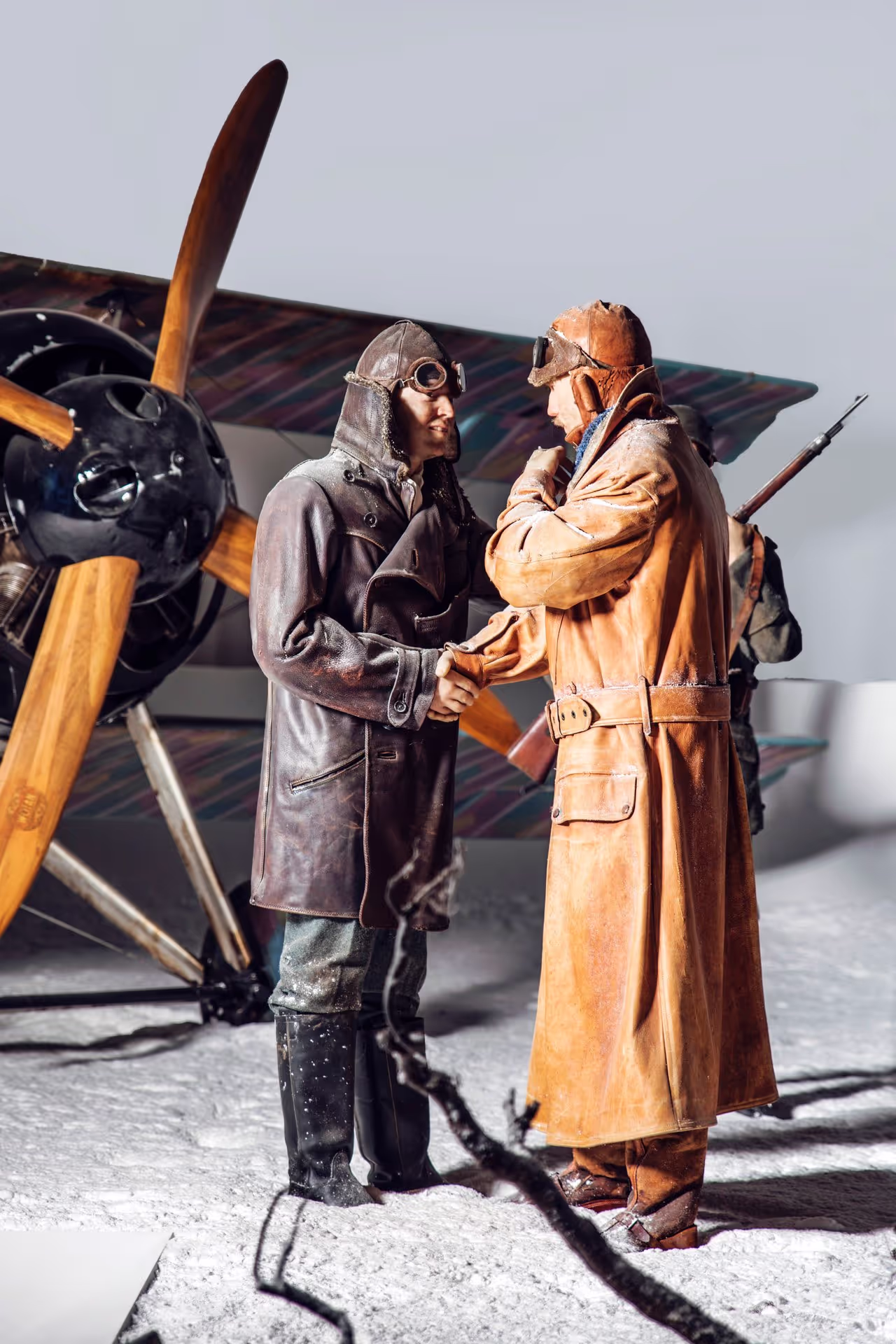 Two vintage pilots in leather flight gear standing by a propeller plane.