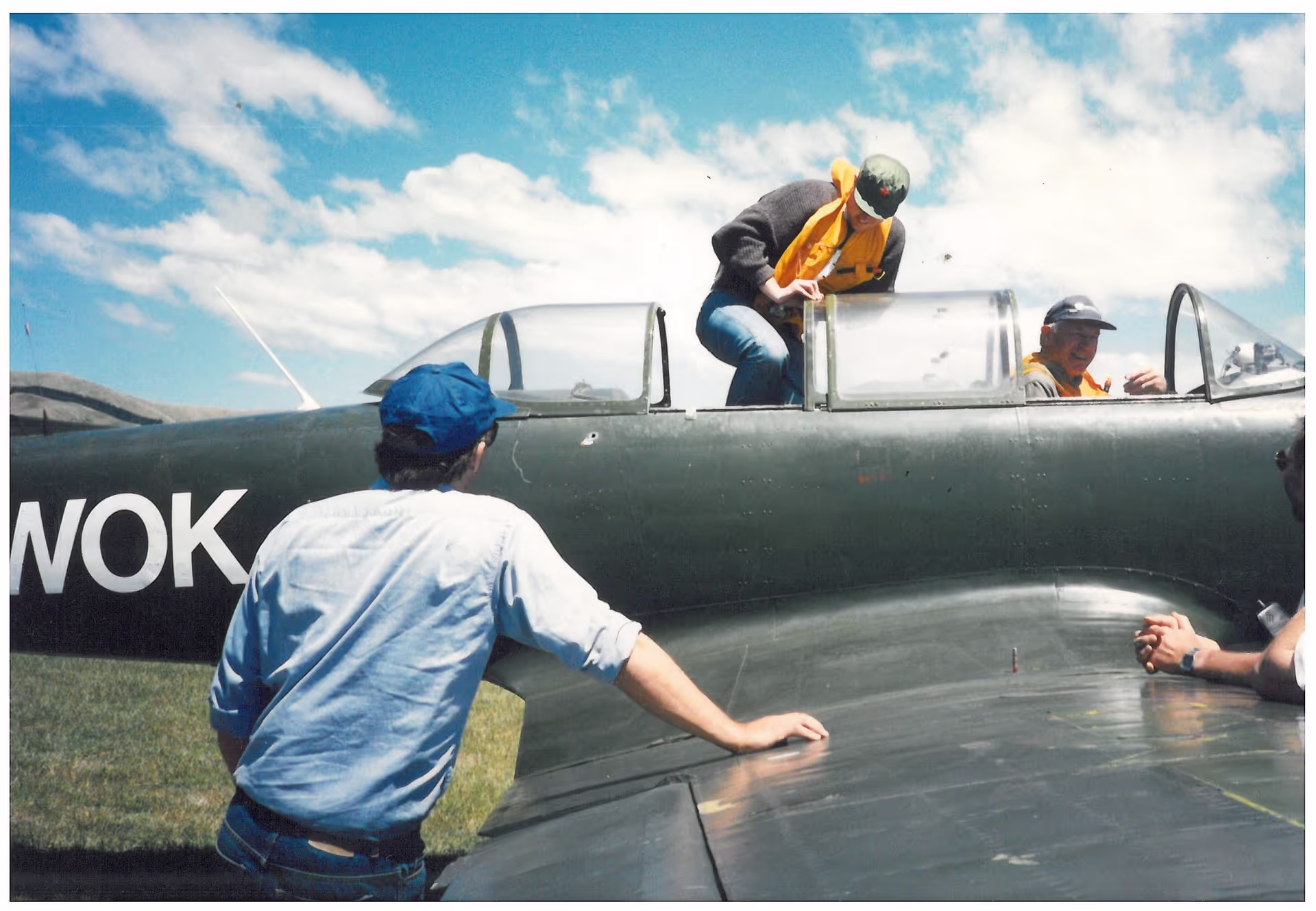 Two people working on a vintage aircraft under a blue sky.