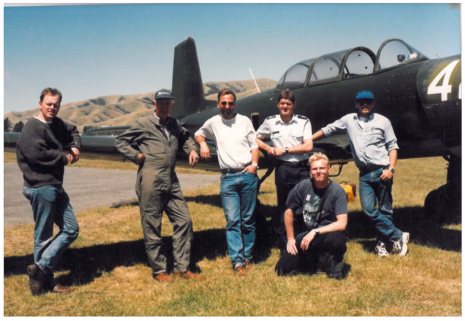 Group of people posing with a vintage aircraft on a sunny day.