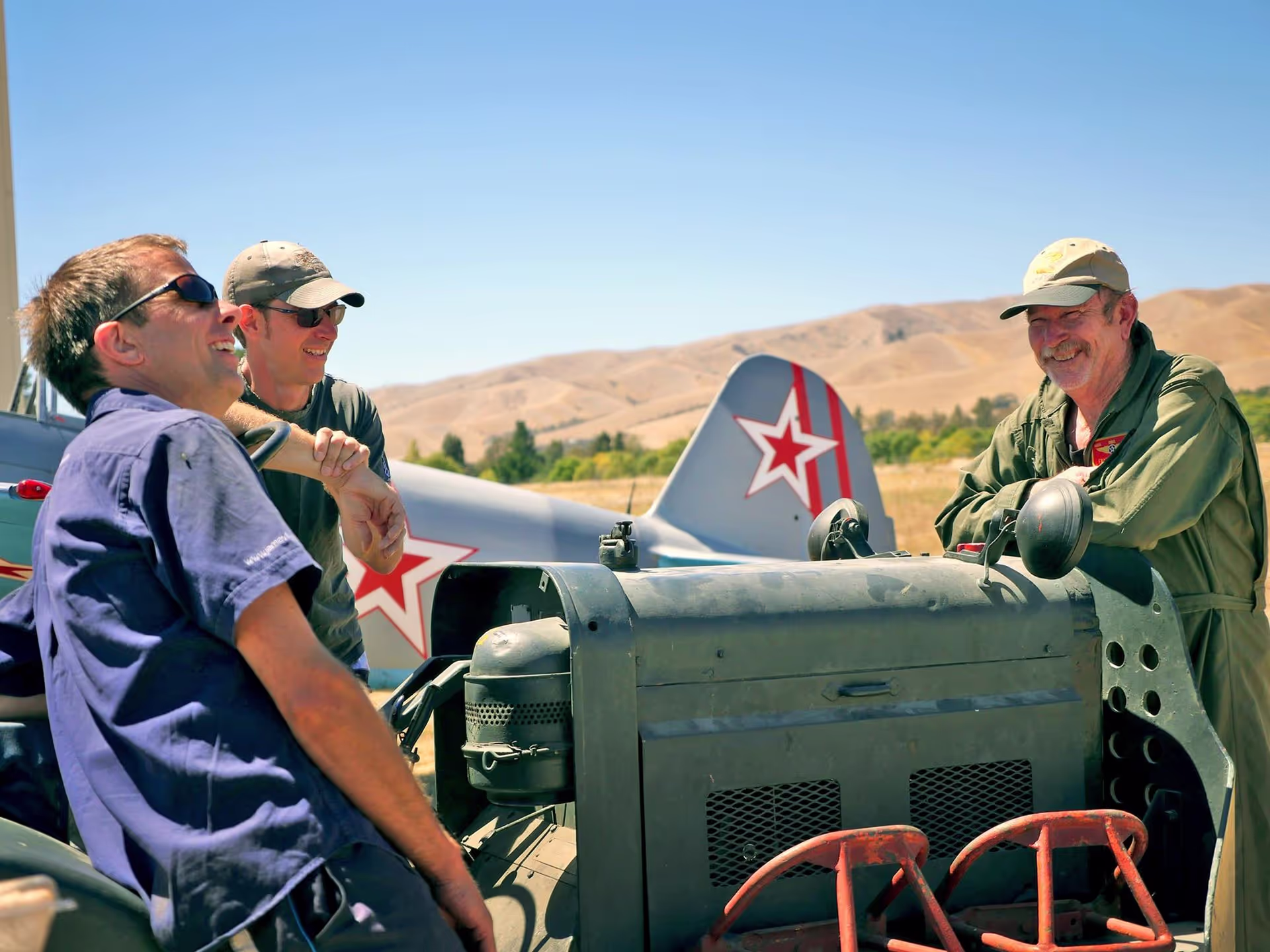 Three people in military attire next to a vehicle with a red star emblem.