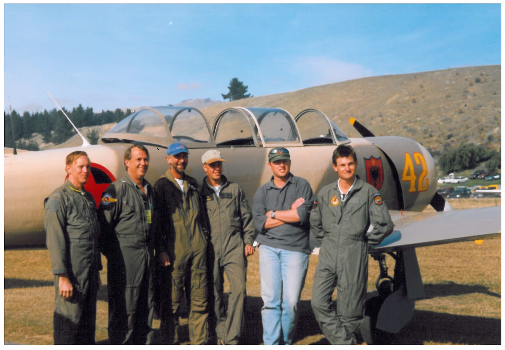 A group of people in flight suits standing beside a propeller-driven aircraft with number 42.