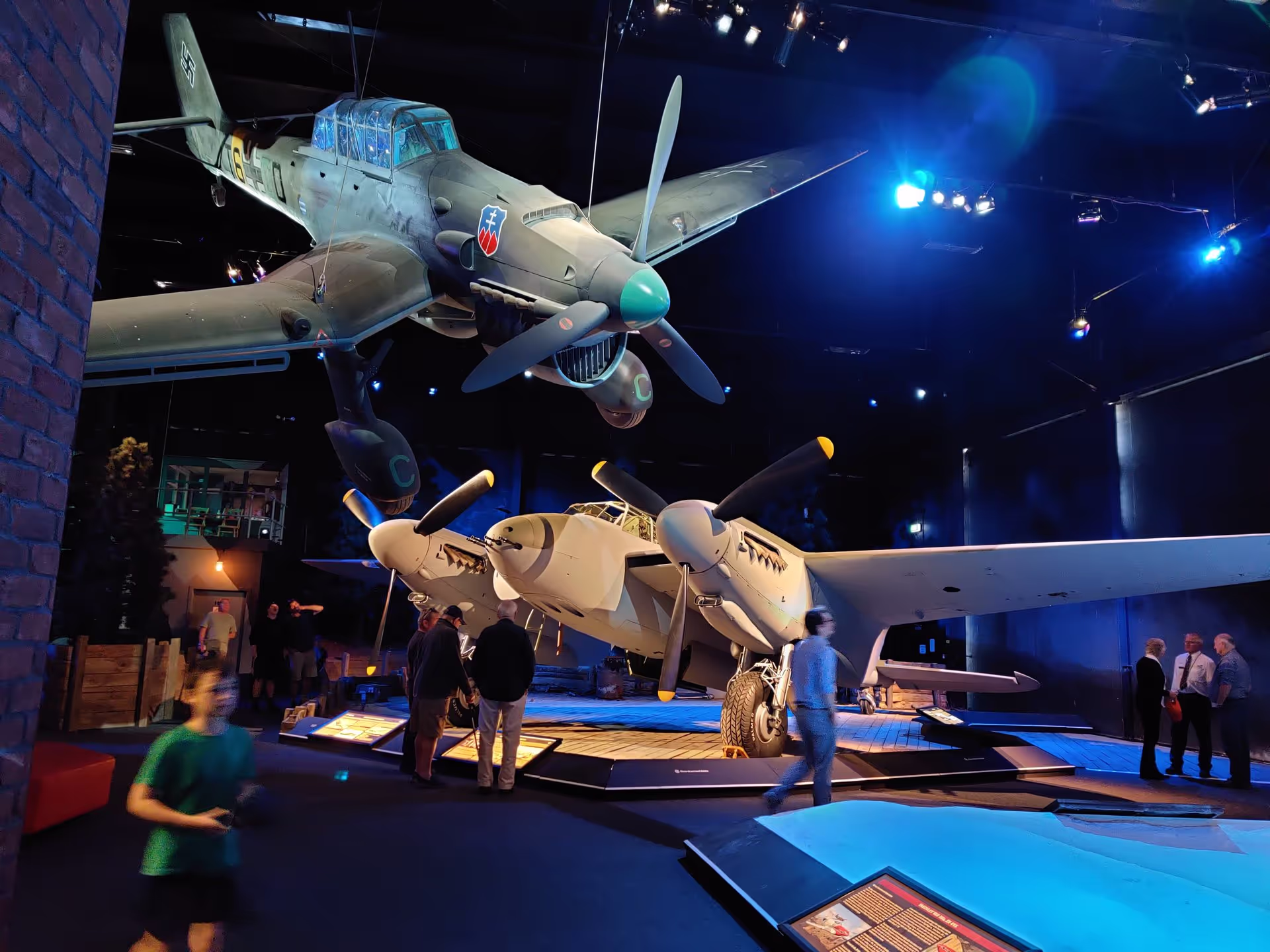 Vintage aircraft on display in a dimly lit museum with visitors walking around.