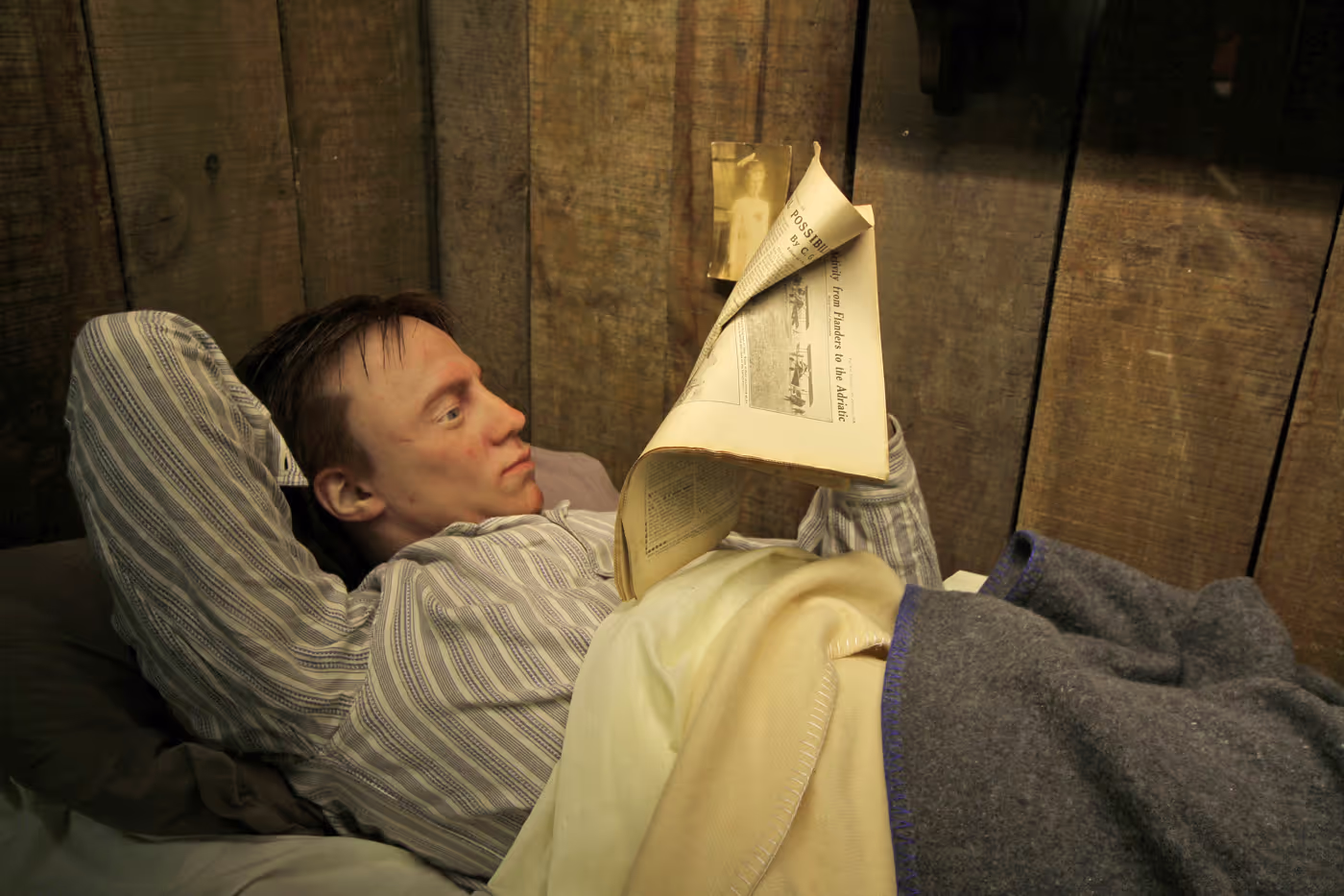 Person lying in bed reading a newspaper, with a wooden background.