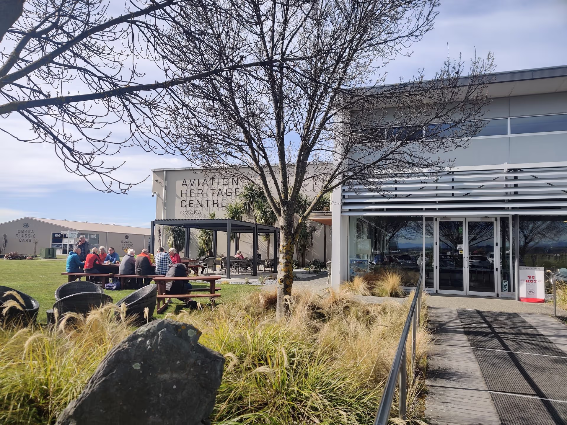 People sitting outside Omaka Aviation Heritage Centre on a sunny day.