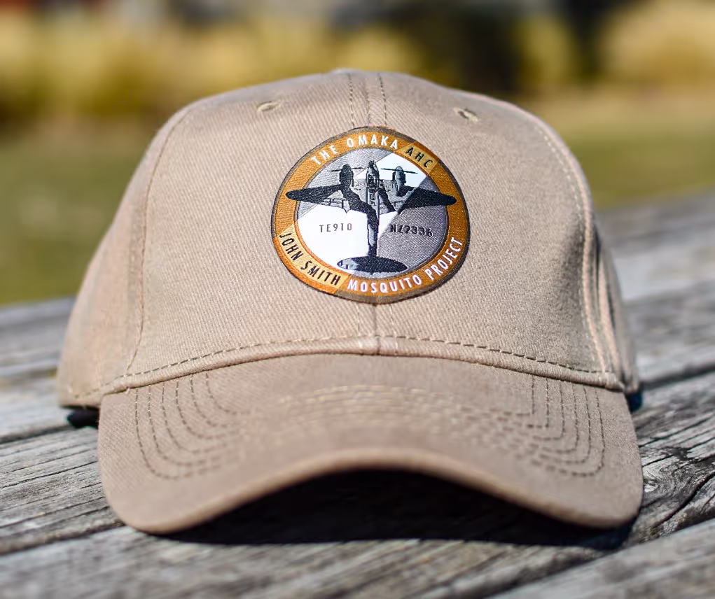 A tan baseball cap with a vintage Omaka Aviation Heritage Centre patch on it, resting on a wooden surface.