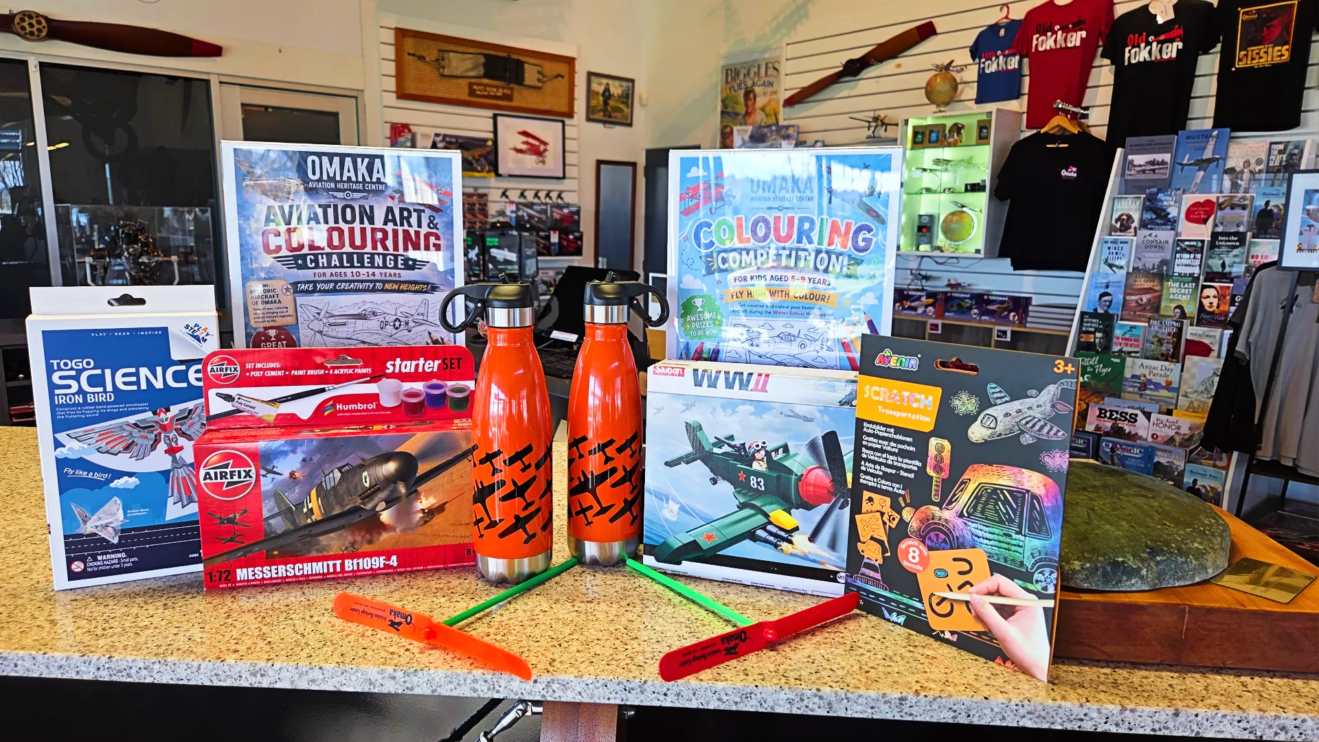Prizes for Omaka Aviation Heritage Centre’s school holiday colouring competition displayed in the museum shop, including aviation-themed model kits, drink bottles, toys and colouring posters.