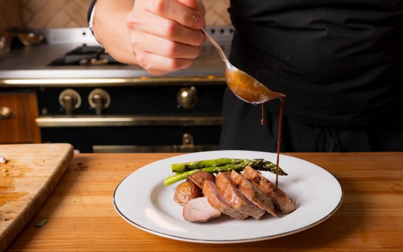 Dark sauce being poured from a spoon over a plated dish in a professional kitchen