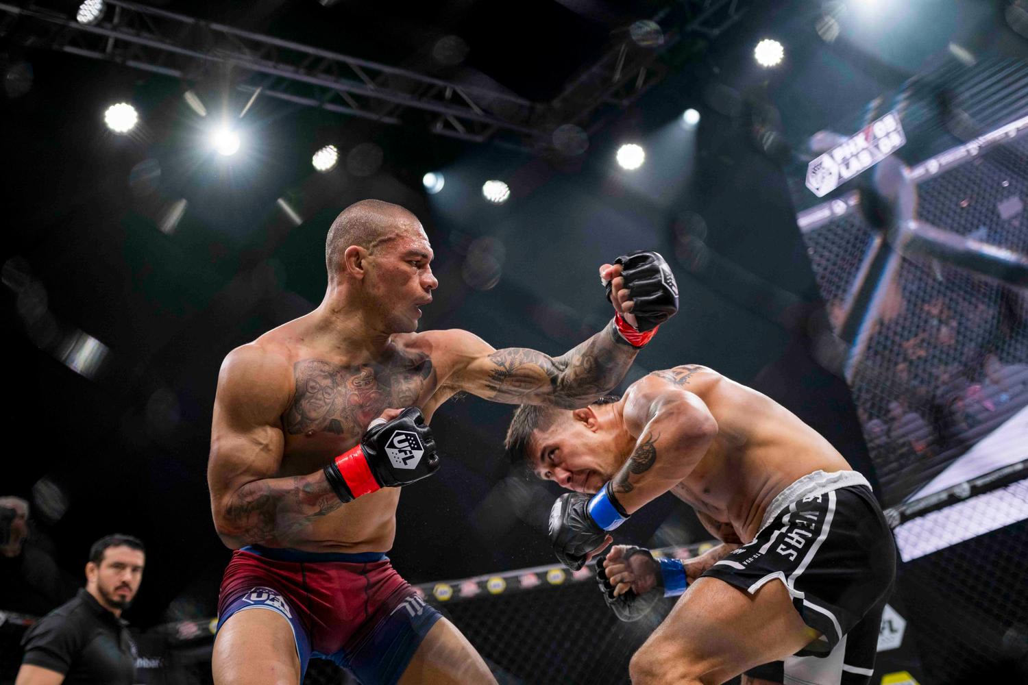 Two MMA fighters engaged in combat inside a cage with one throwing a punch while the other reacts. The scene is captured under bright stage lighting with an octagon cage visible in the background and a referee watching from the side.