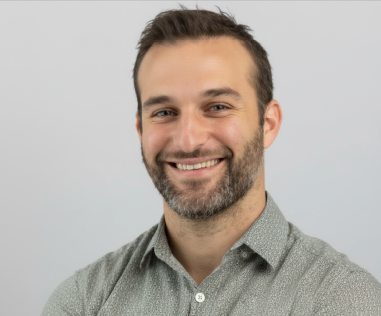 Smiling man with short dark hair and beard wearing a green button-up shirt against a light gray background.