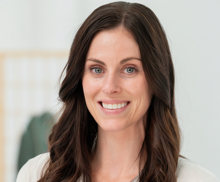 Smiling woman with long dark brown hair wearing a light blue shirt against a blurred indoor background.