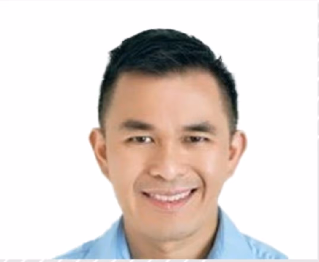 Portrait of a smiling man with short dark hair wearing a light blue shirt against a white background.