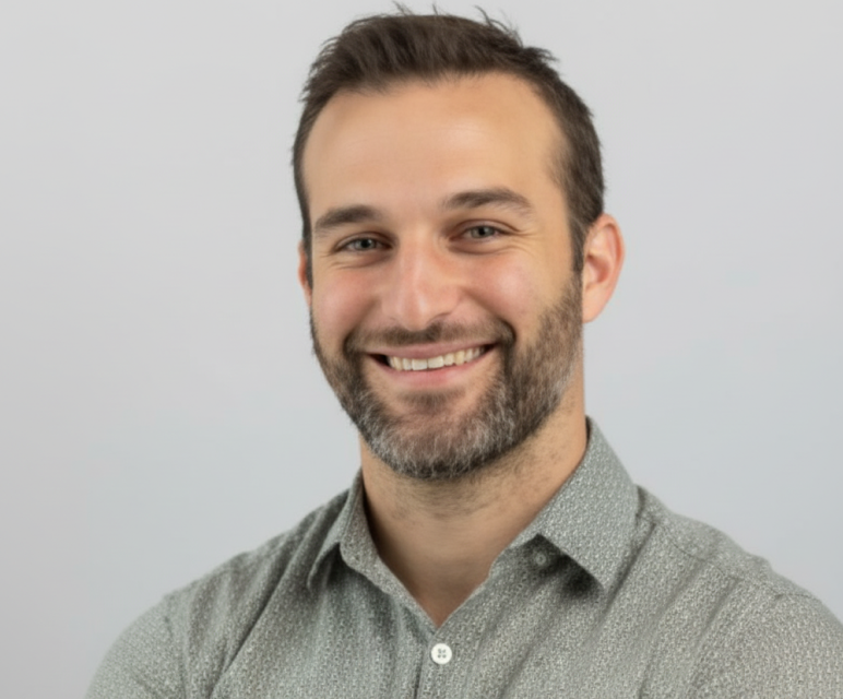 Smiling man with short brown hair and beard wearing a light gray patterned button-up shirt.