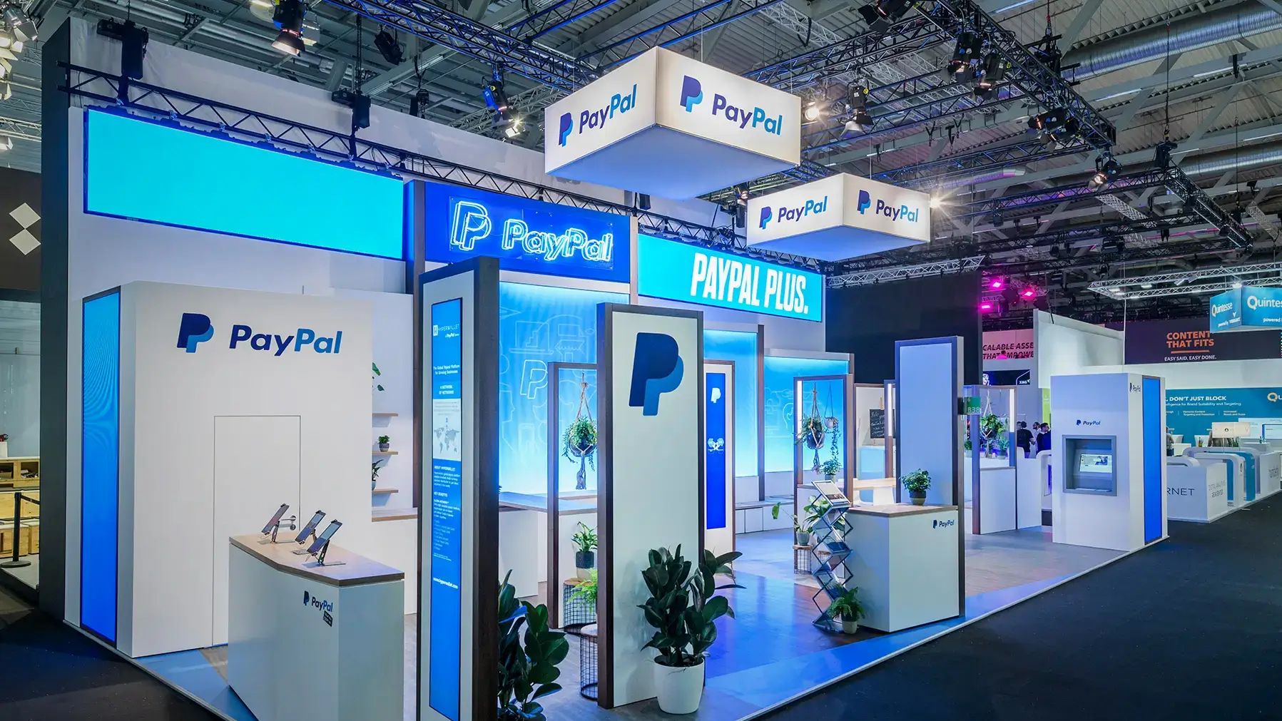 Übersicht des PayPal DMEXCO Messestands, Agentur fivekit, modernes B2B-Design mit großzügigen Flächen, Pflanzen und digitalen Screens.