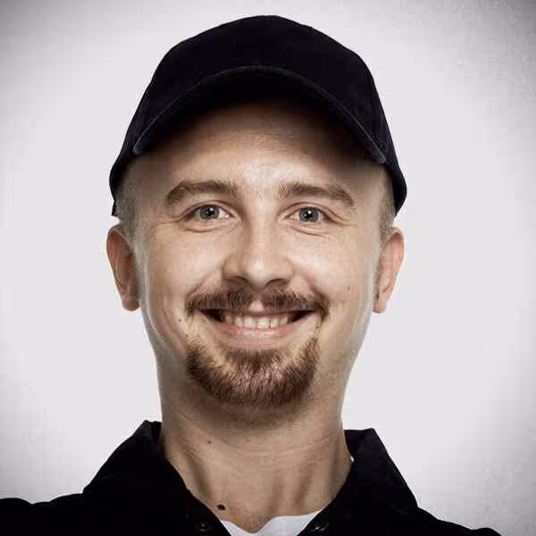 A smiling man with a beard wearing a cap, exuding a friendly and approachable demeanor.