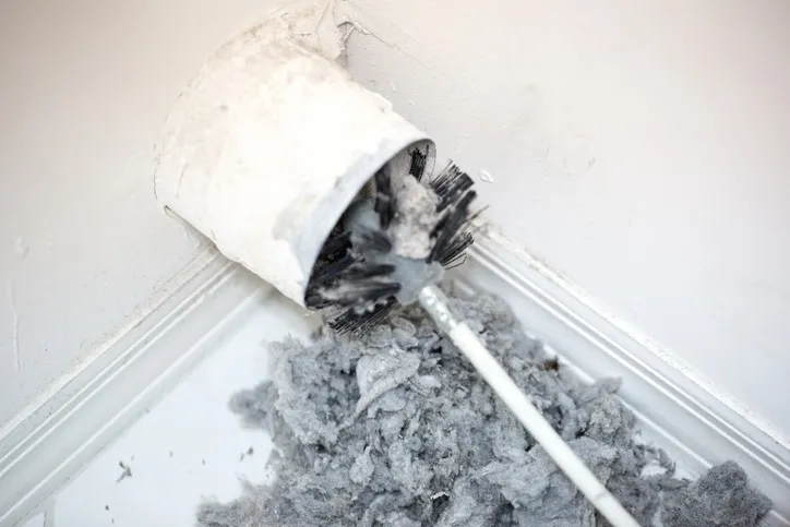 A brush is cleaning a dryer vent, with a large pile of lint visible.