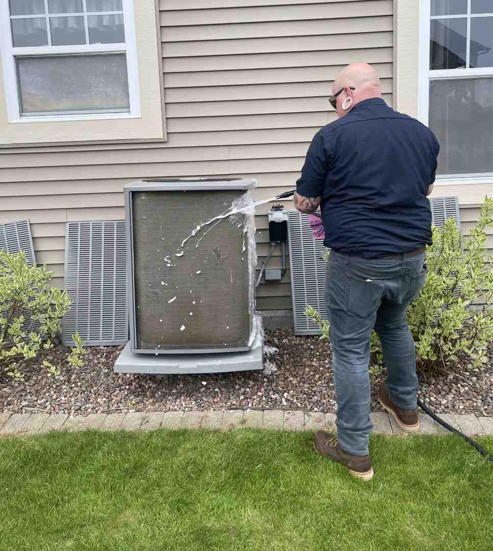 homeowner clearing leaves and debris from outdoor HVAC unit with gloves - spring hvac transition from heating to cooling