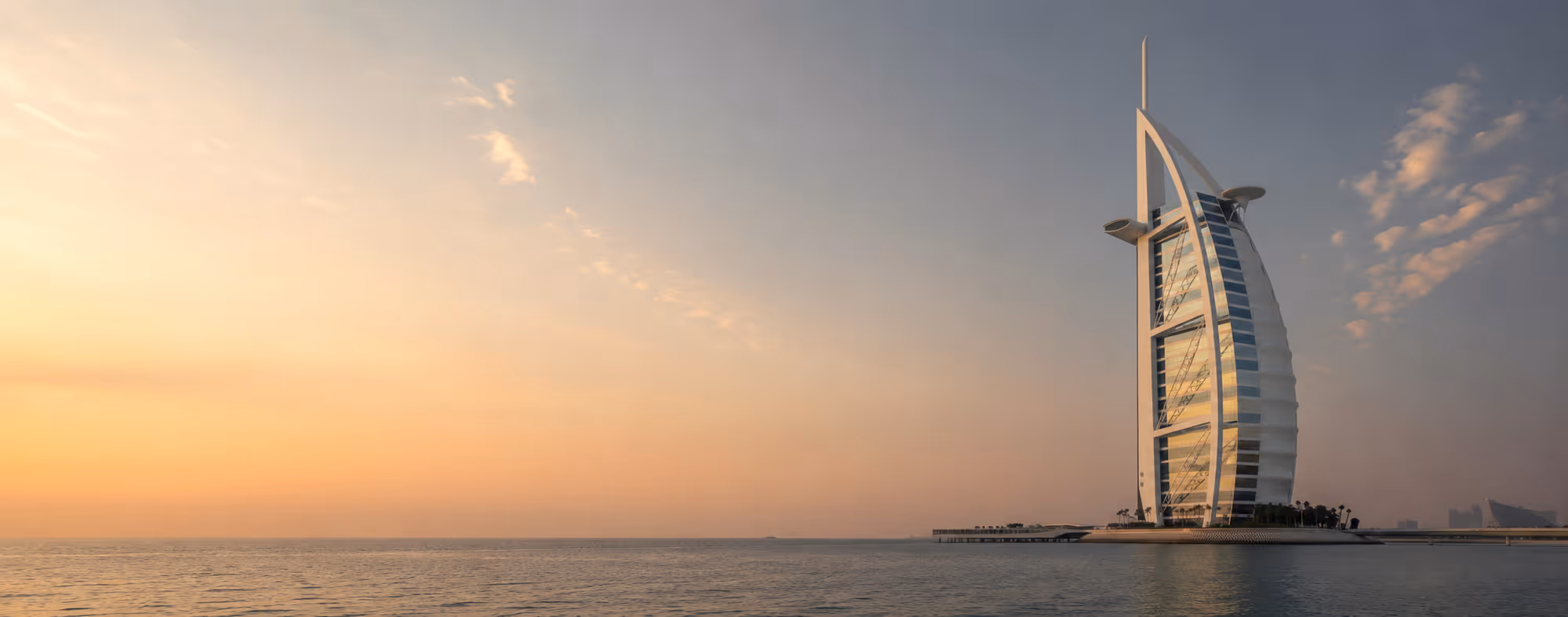 Burj Al Arab hotel standing on a man-made island during a calm sunset over the sea.