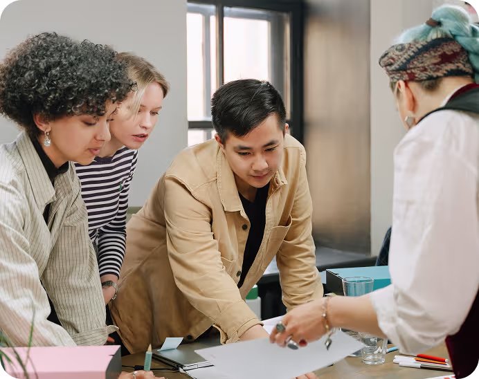 Four diverse young adults gathered around a table reviewing documents in a bright office.