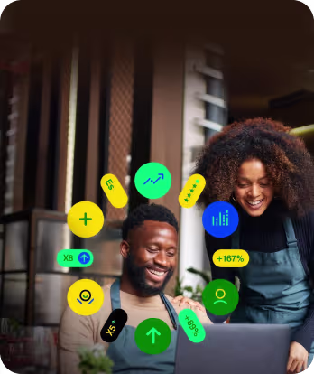 Two smiling people wearing aprons looking at a laptop with colorful finance icons around them.