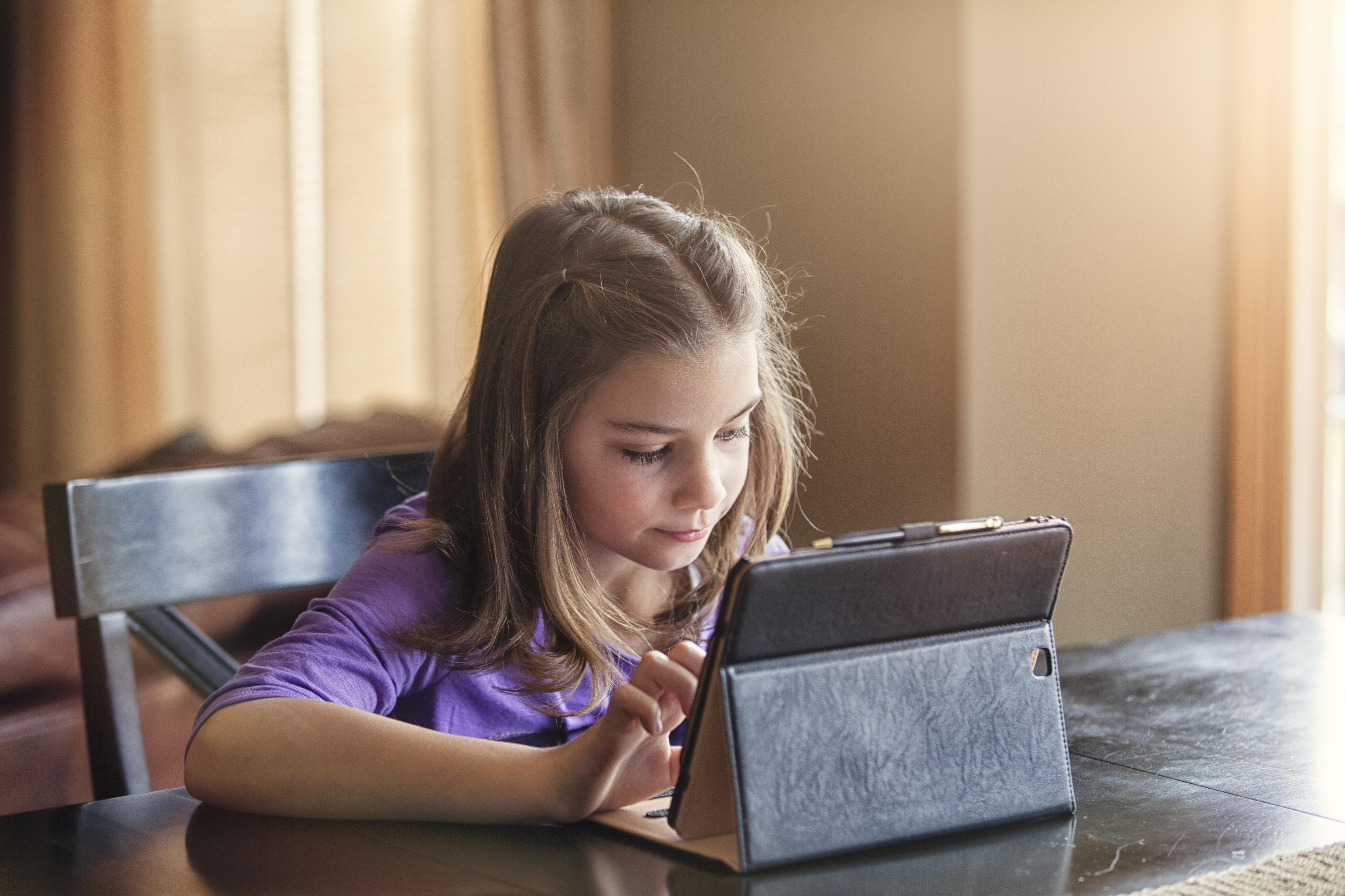 Girl using a tablet device at a wooden table for homeschool learning