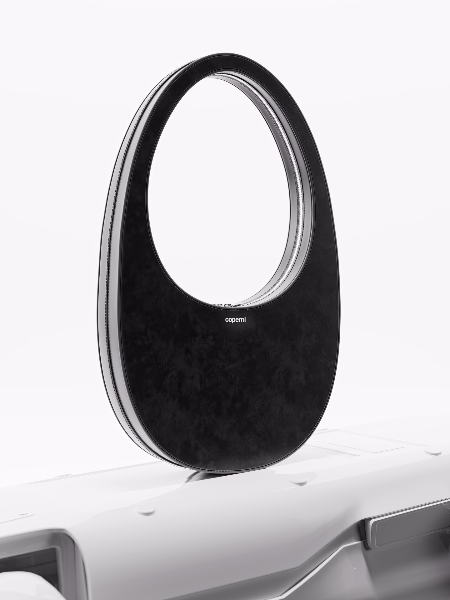 Black oval-shaped handbag with a cutout handle and zipper detail by Coperni on a white surface.