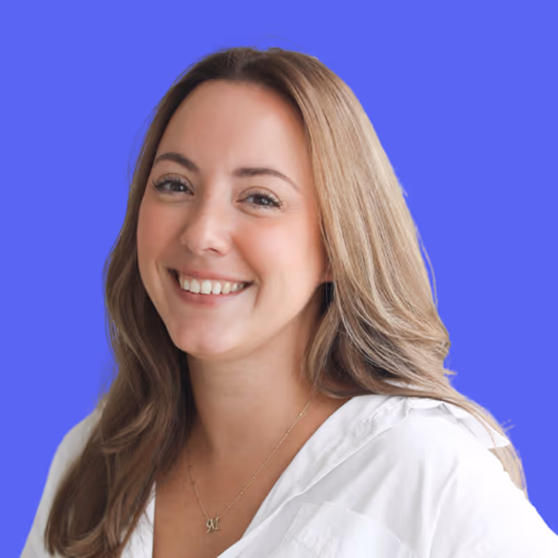 Smiling woman with light brown hair wearing a white blouse and a necklace against a blue background.