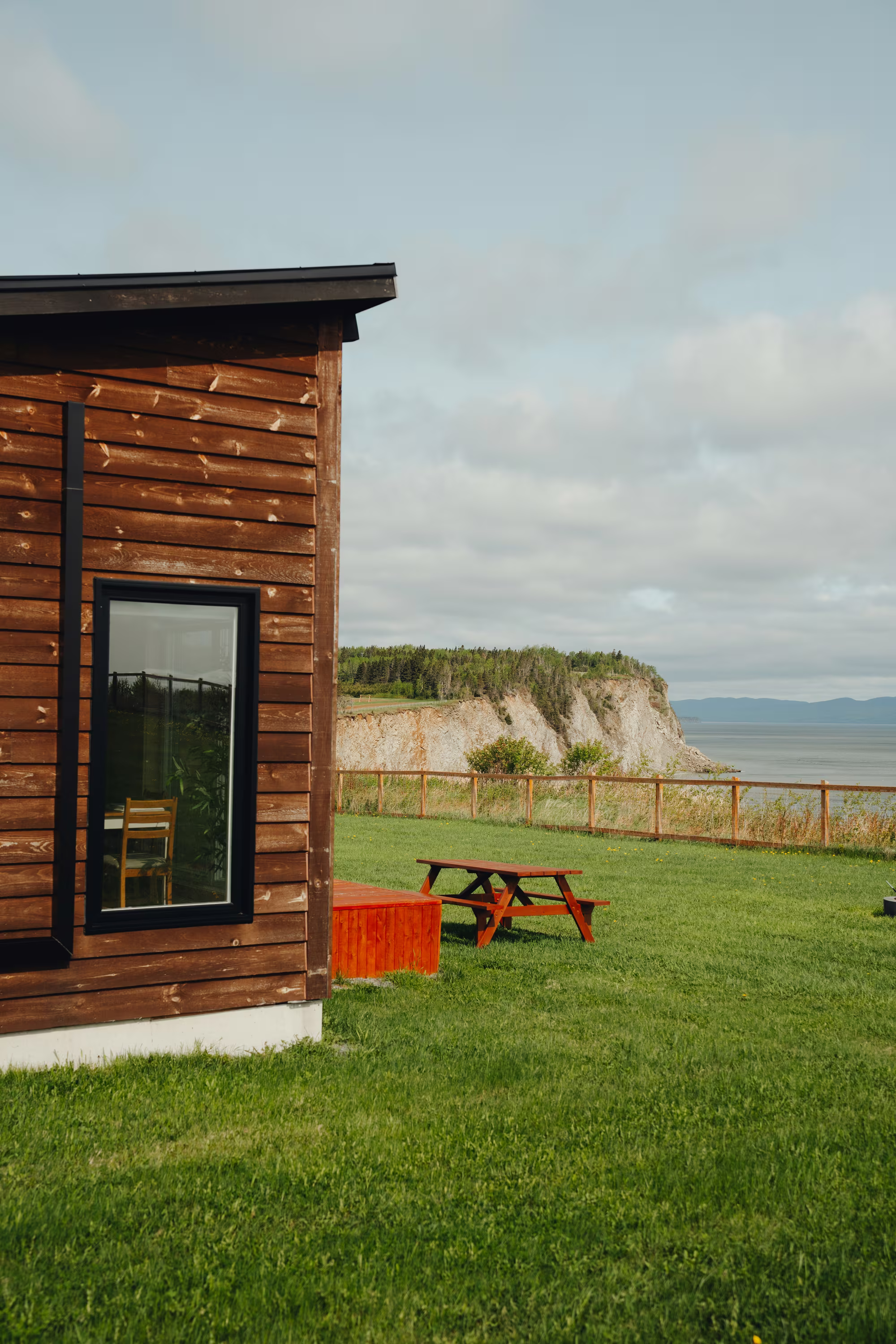 Chalet avant à revêtement de bois foncé sur la pelouse, falaise et mer en arrière-plan