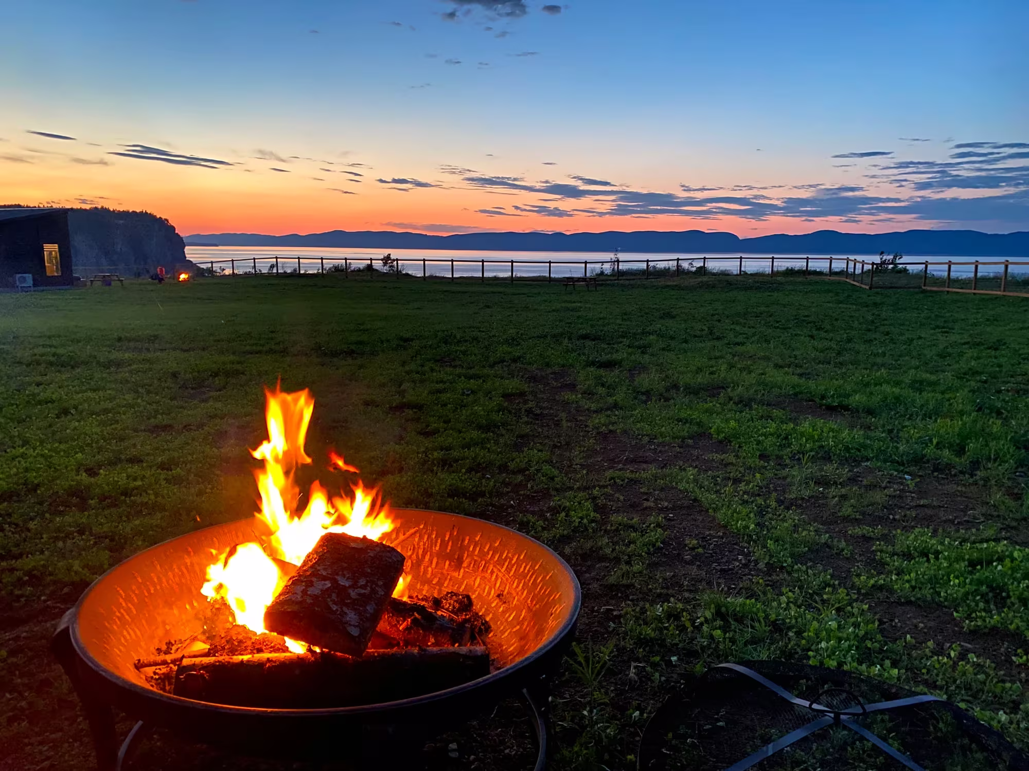 Foyer extérieur allumé sur la pelouse au crépuscule, face à la baie de Gaspé