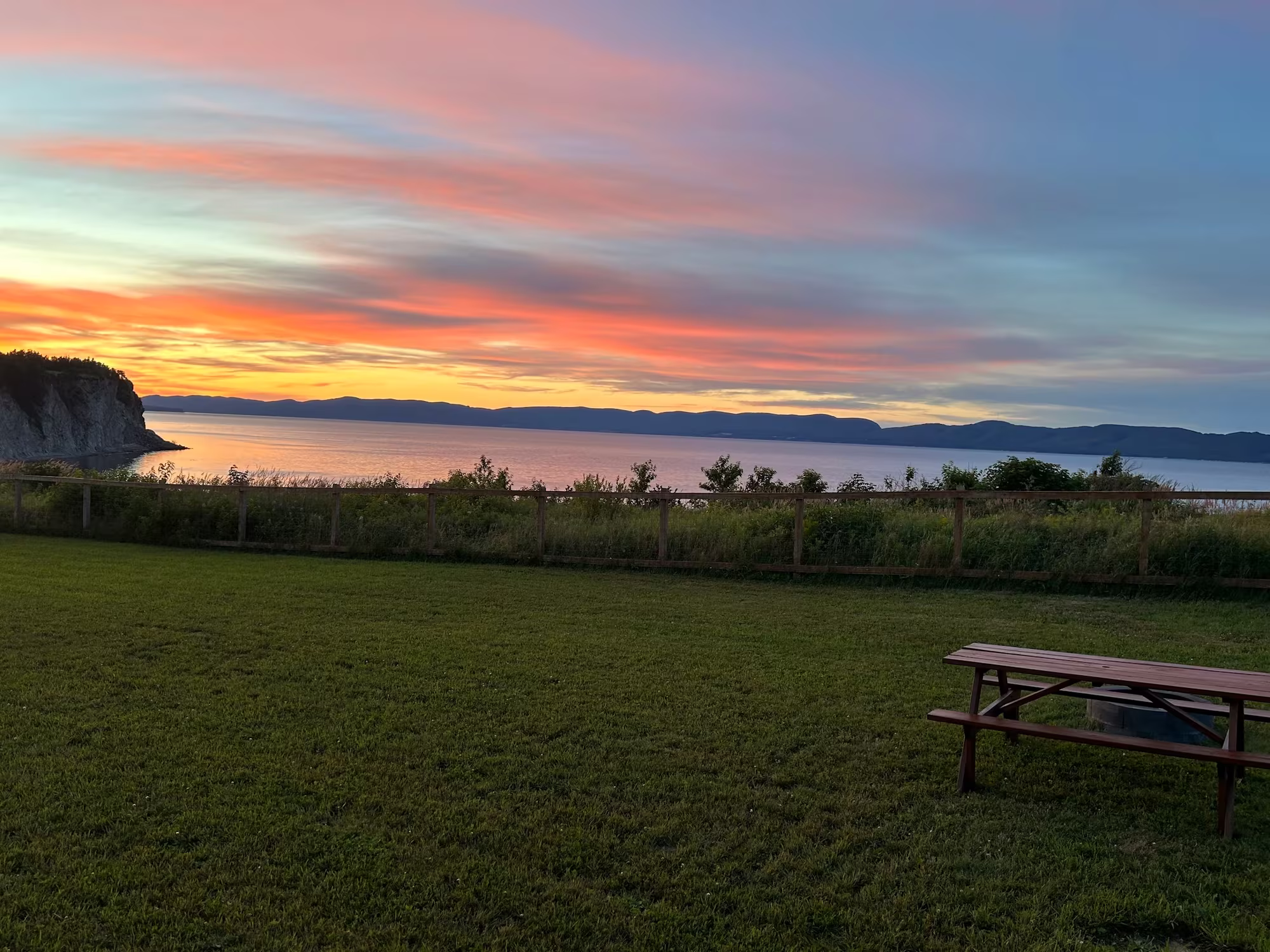 Table à pique-nique sur la pelouse face à la baie de Gaspé au coucher du soleil