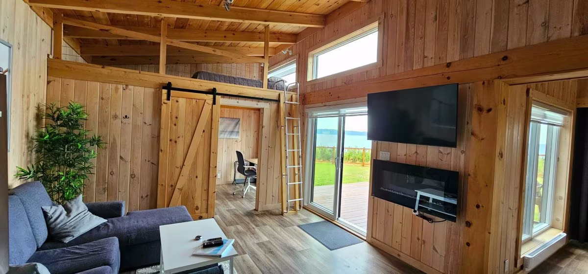 Le séjour avec téléviseur, porte-grange et mezzanine à l'étage du chalet double avant