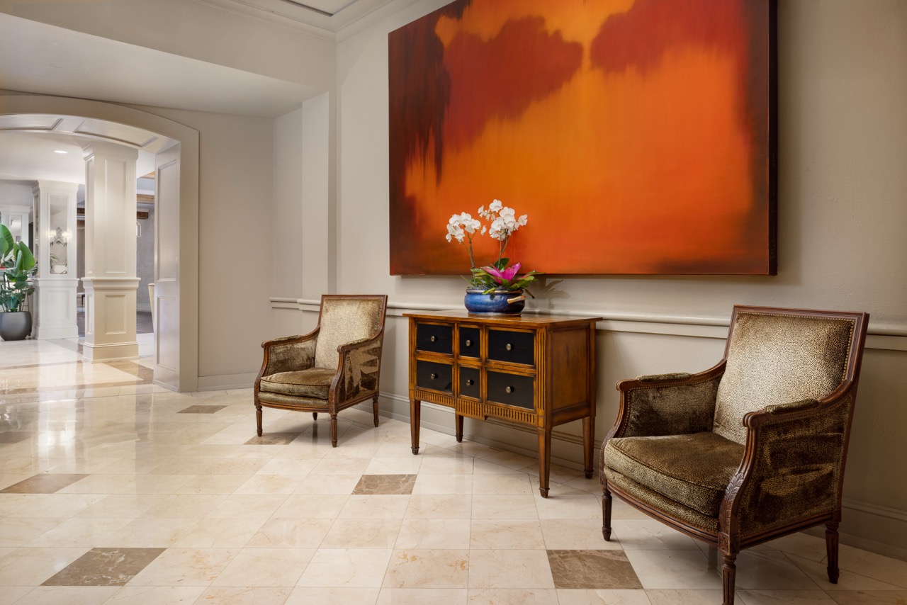 Two seats with large orange hue artwork on wall in hallway