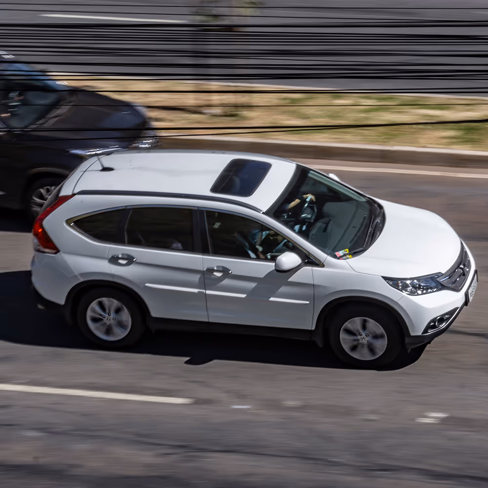 White SUV with sunroof driving on a city street next to a black vehicle.