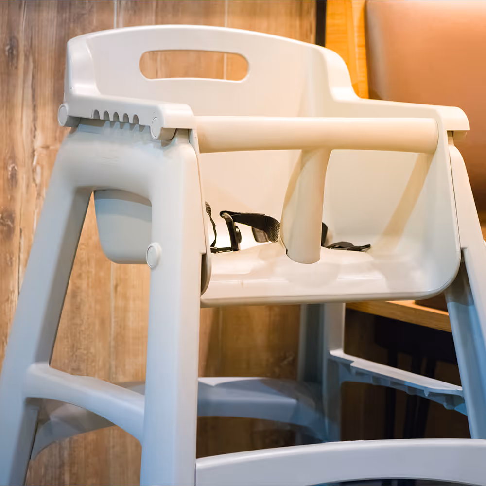 White plastic high chair with a safety harness and a wooden background.