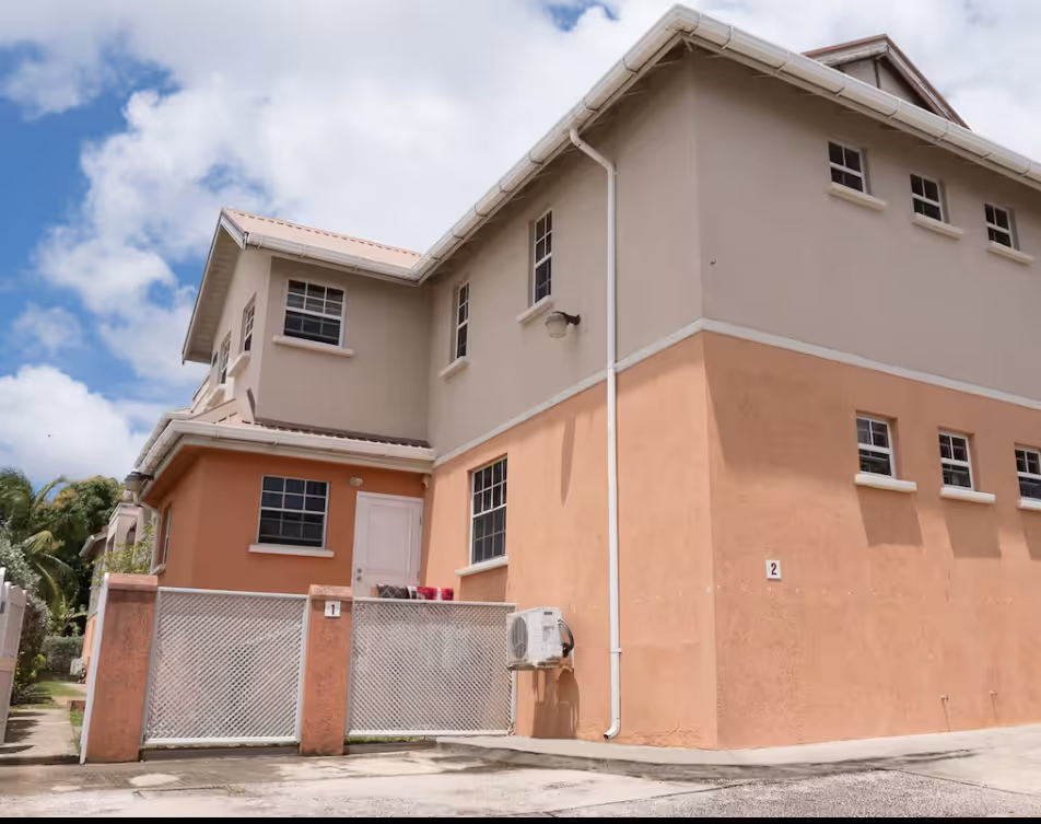 Two-story house with beige and peach exterior, metal gate, multiple windows, and an air conditioning unit mounted outside.