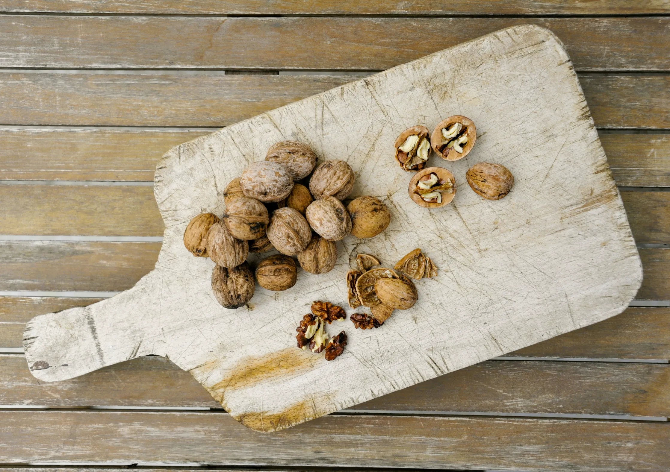Rustic board with whole walnuts and cracked walnut halves arranged to show rich brown shells and golden interiors. Natural light emphasizes texture and quality, reflecting Sharon Naraghi Farms’ careful California cultivation and post-harvest handling for premium flavor.