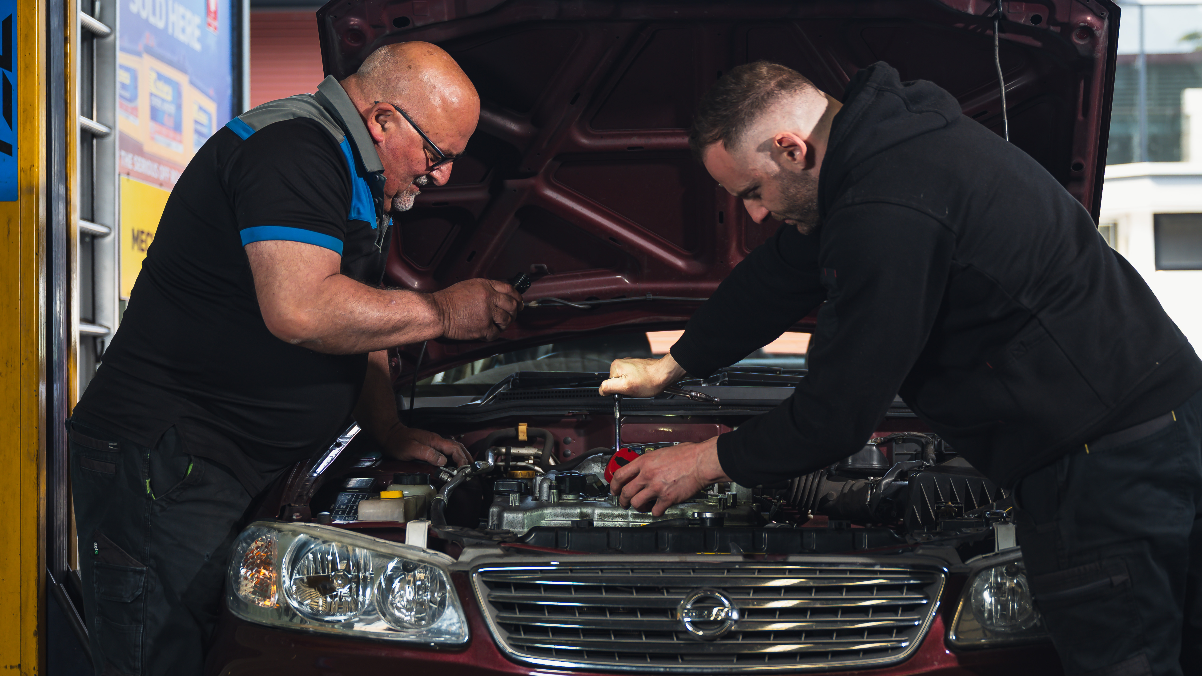 Christopher and John in Modbury Motors are inspecting a vehicle during a service and tightening the spark plugs