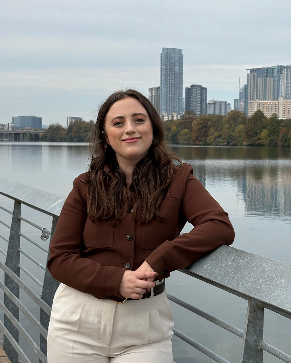 Austin-based Sex Therapist Brooke Becker leaning on a railing by the river and smiling