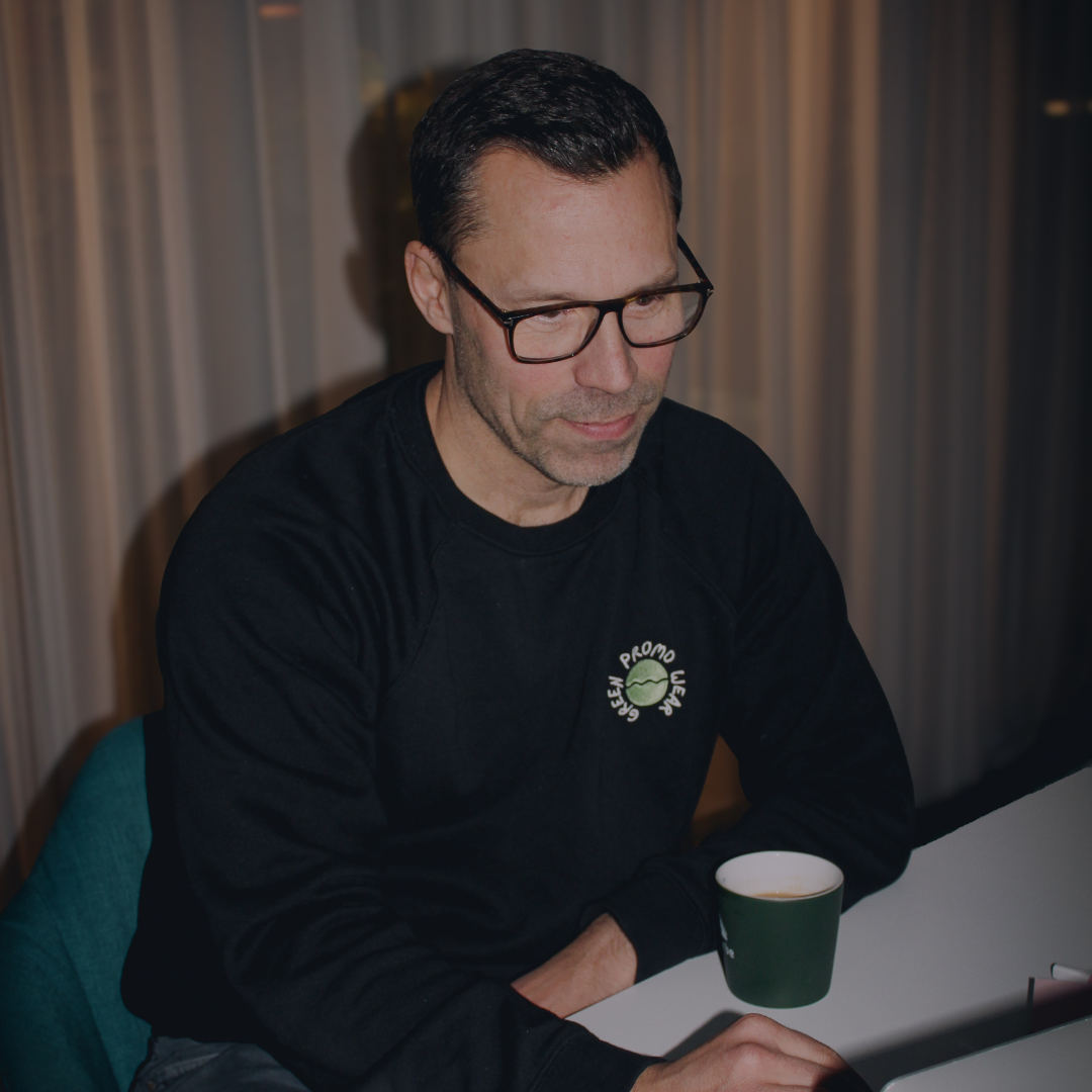 Man wearing glasses and a black sweatshirt sitting at a table with a green cup.