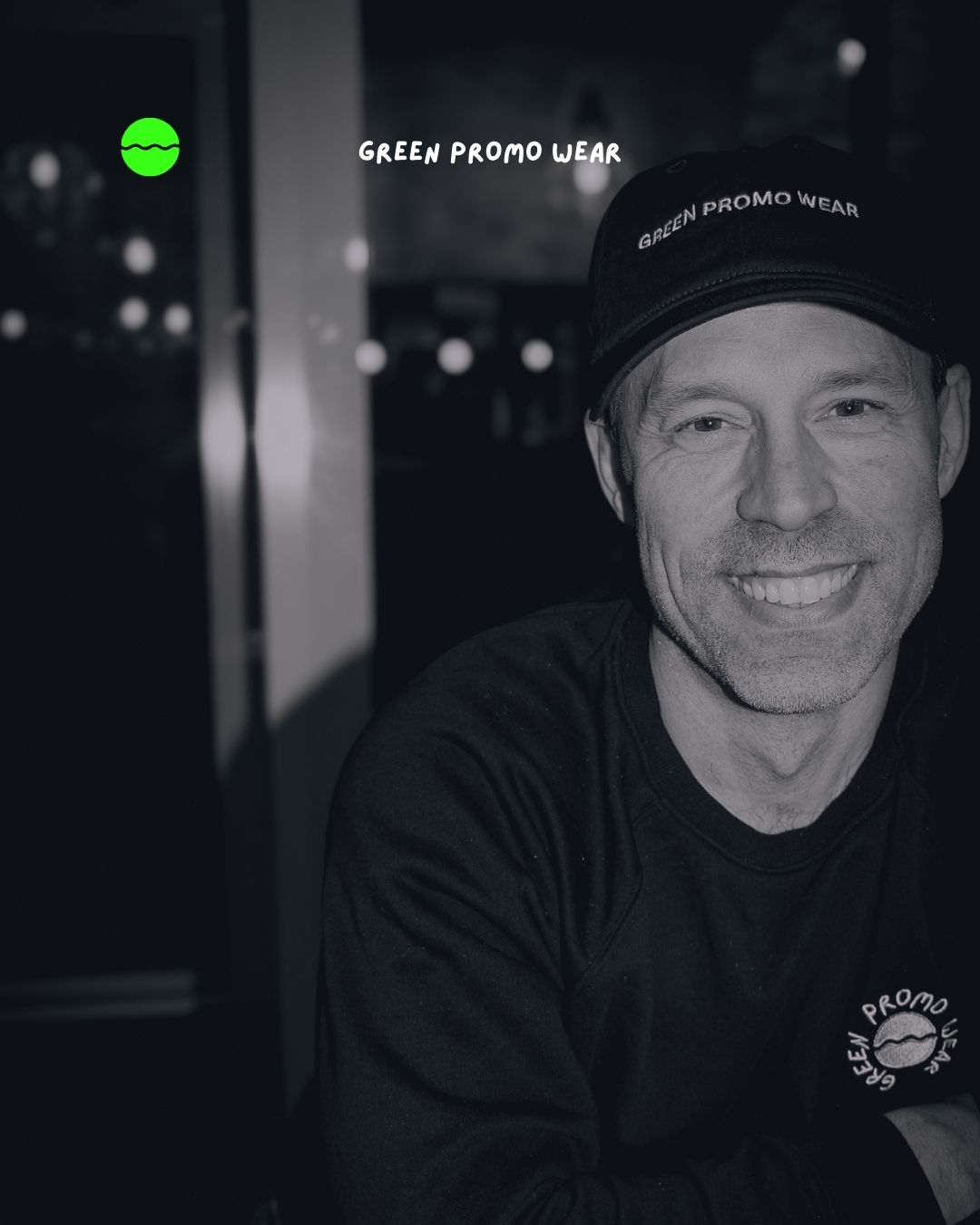 Smiling man wearing a black cap and sweatshirt with 'Green Promo Wear' logo and text.