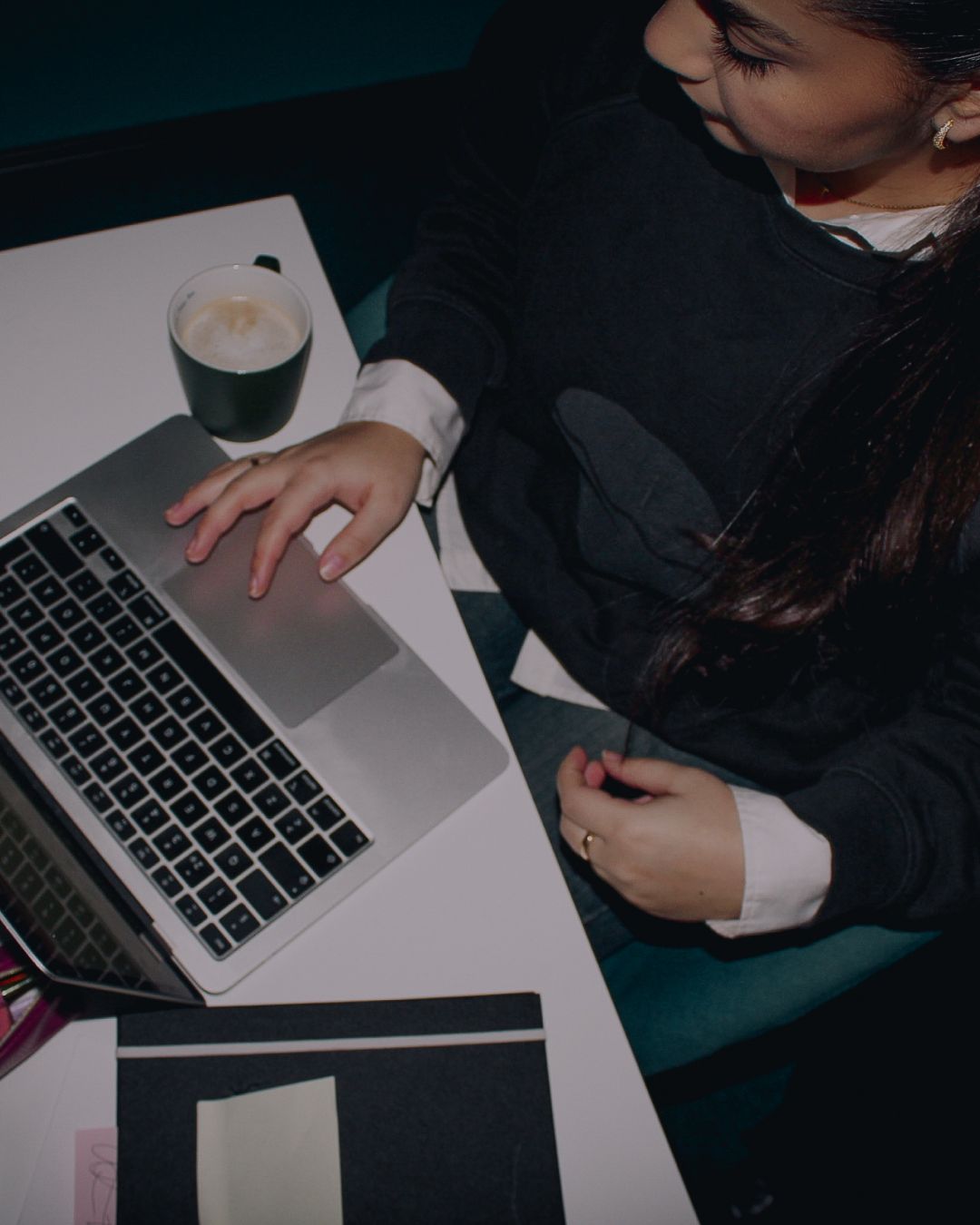 Person using a laptop at a white desk with a cup of coffee nearby.