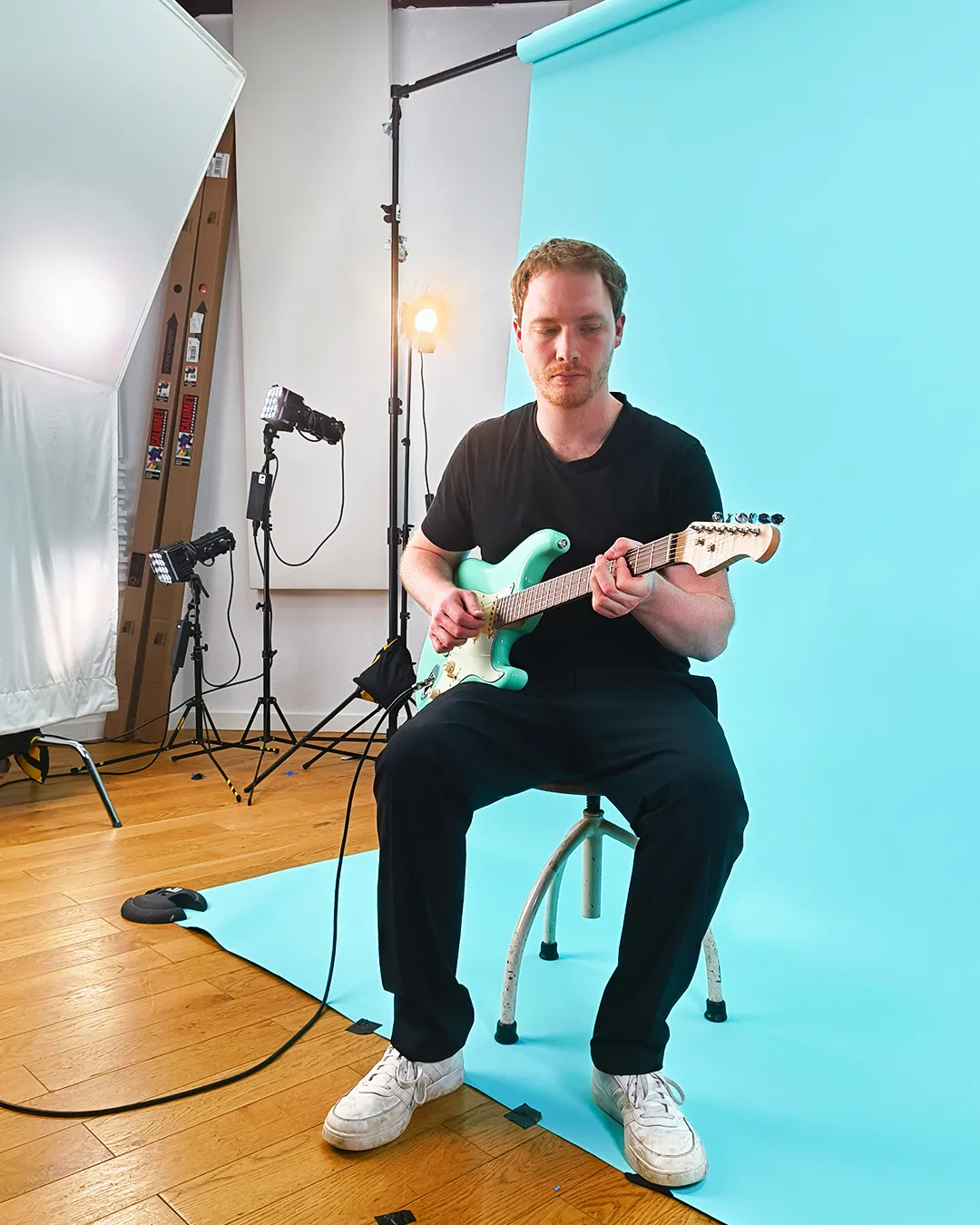 Julius Imhäuser sitzt mit türkiser Gitarre vor einem türkisen Backdrop
